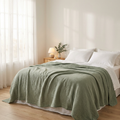 Solvrly Cloud Gauze Coverlet in Sage Green on a bed in soft morning light