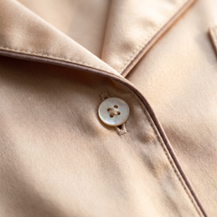 Close-up of champagne silk fabric with mother-of-pearl button and piping