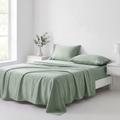 Sage green cooling silk sheet set made up on a bed in a bright bedroom
