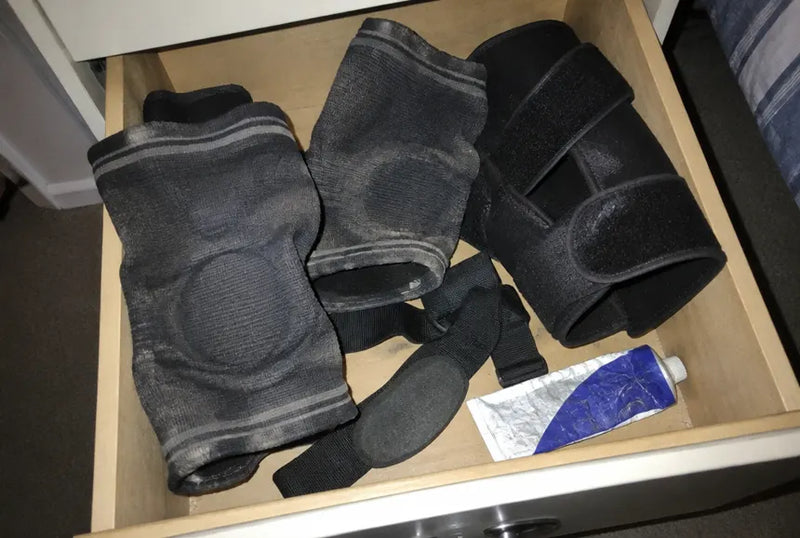 An open drawer holding a tangle of abandoned knee sleeves, wraps and a flattened cheap strap